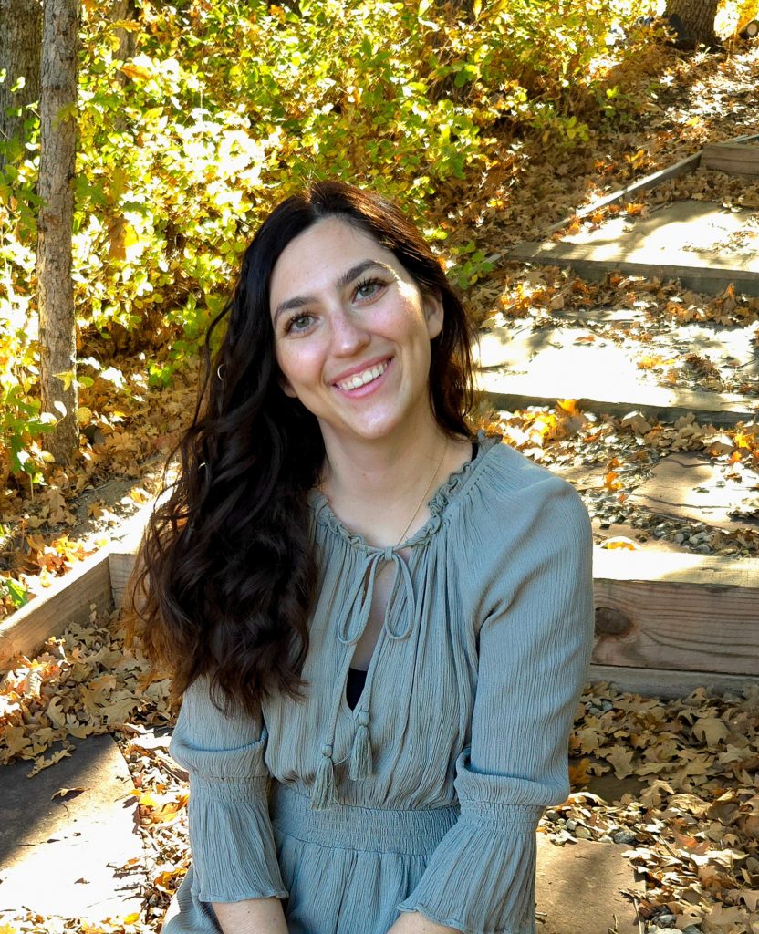 Image of Ally Meisner sitting in a wooded area smiling at the camera