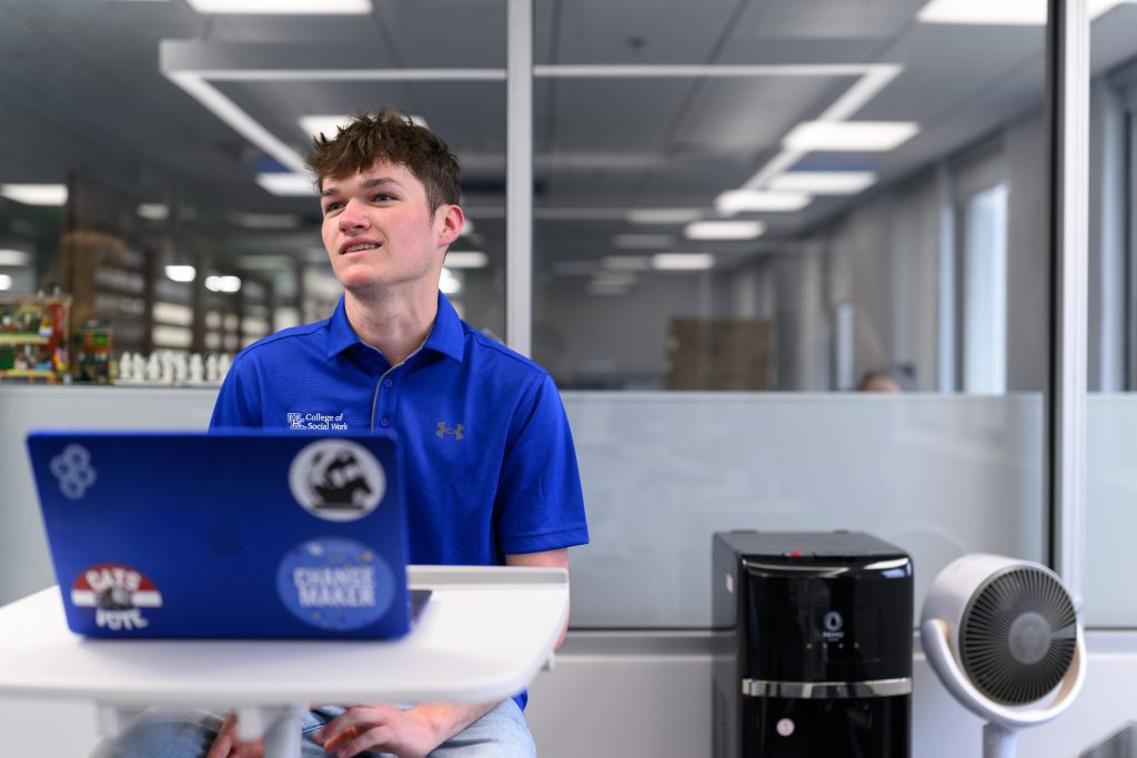 Student Ben Ison smiling while sitting in front of his computer in the moving meeting room