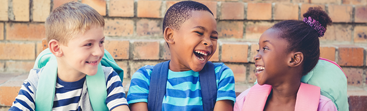 Three young kids wearing backpacks and smiling and laughing