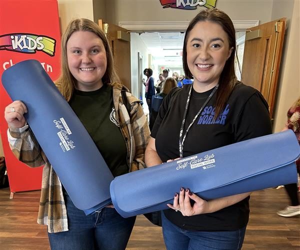 Two Alumni hold Self Care yoga mats from COSW event
